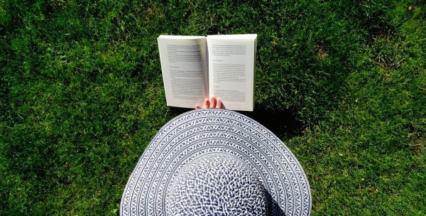 A top-down view of a woman's large hat and a book set against green grass